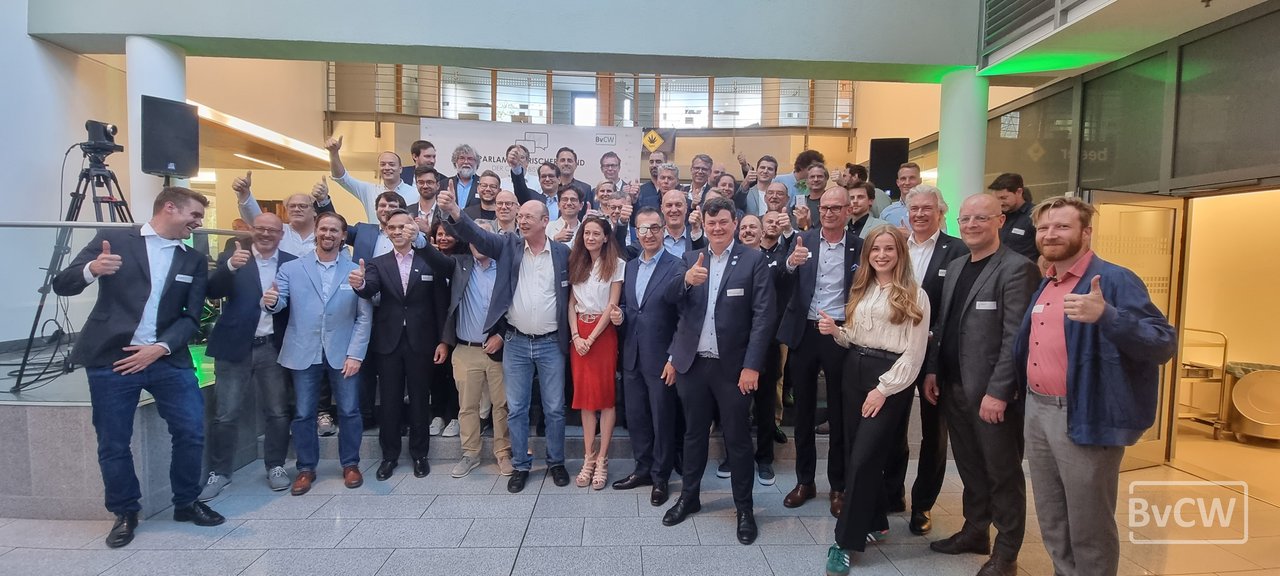 Some forty people lined up for a group photograph in a bright foyer, many giving a thumbs-up. Behind them a banner reading Parlamentarischer Abend der Cannabiswirtschaft with the BvCW logo.