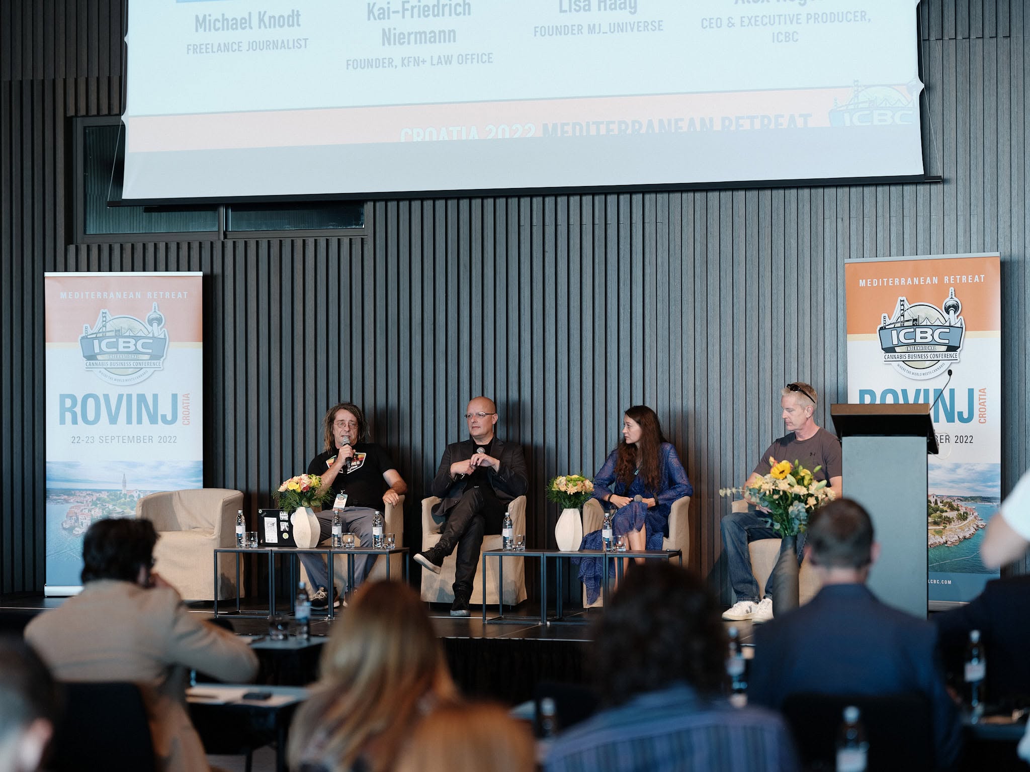 A panel on stage in front of an audience, with ICBC's logo and the word ROVINJ on the screens. Above the stage a banner with four names and titles: Michael Knodt, freelance journalist; Kai-Friedrich Niermann, founder KFN+ Law Office; Lisa Haag, founder MJ_UNIVERSE; Alex Rogers, CEO and executive producer, ICBC.