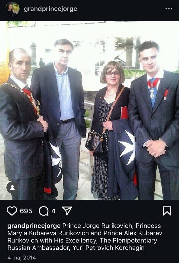 Screenshot of an Instagram post: four people outdoors, two of them holding folded black mantles with a white cross.