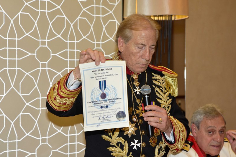 A man in a gold-embroidered uniform holds up a certificate with the UN emblem and the text United Nations.